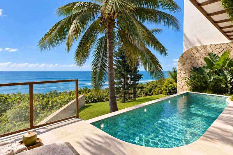 Piscina privada bajo una palmera con el océano al fondo
